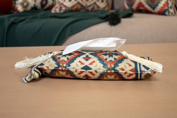 Ethnic-patterned tissue box cover placed on a wooden side table in a cozy living room.