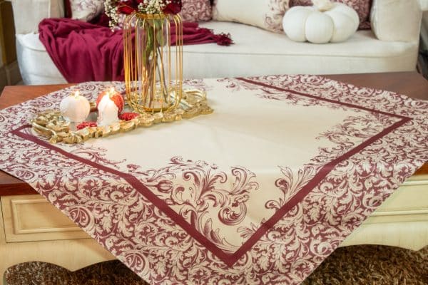 Burgundy square tablecloth styled on a coffee table with floral decor and candles.