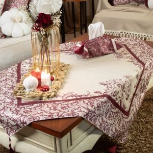 Burgundy square tablecloth styled on a coffee table with floral decor and candles.