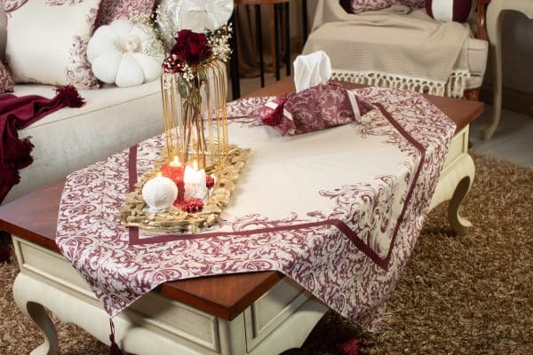 Burgundy square tablecloth styled on a coffee table with floral decor and candles.