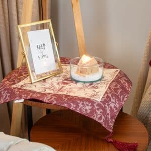 Burgundy side table cloth styled with matching decor accents and a small vase.